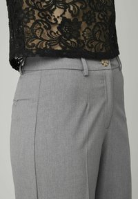 Pantalons gris ajustés en tissu lisse, avec une fermeture à bouton, des passants de ceinture et des poches latérales. Présentés avec un haut en dentelle noire.
