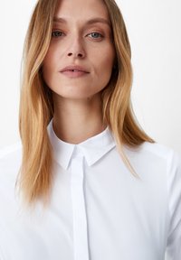 Camicia bianca con colletto e bottoni frontali, maniche lunghe. Tessuto leggero e morbido con una vestibilità normale. Design minimalista.