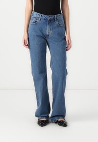 Light blue denim jeans with a relaxed fit, high waist, five-pocket design, and contrasting stitching. Worn with black pointed flats.