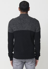 Suéter de rayas en negro y gris con cuello alto y acentos en los hombros, que presenta un patrón texturizado en la mitad superior.