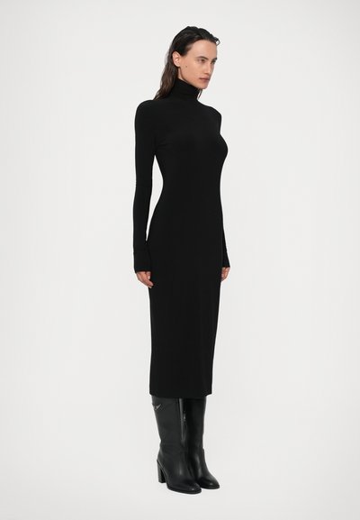 Črna obleka s turtleneck izrezom, prilegajoča oblikovana s dolgimi rokavi. Material je gladek in elastičen, sega do sredine meč. V kombinaciji z črnimi škornji do kolen.
