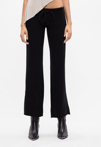 Calças largas pretas com cintura elástica, feitas de material suave. Textura lisa com detalhes mínimos. Combinadas com botins pretos ajustados.