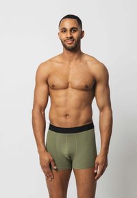 Olivgrüne Boxershorts mit einem schwarzen elastischen Bund, leichtem Baumwollmaterial und einem taillierten Design mit minimalen Nähtdetails.