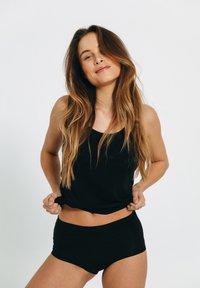 Sort tanktop og matchende shorts i et blødt materiale, med et tætsiddende design og glat tekstur, båret af en model mod en hvid baggrund.