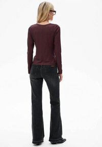 Bordeaux rode langemouwen top met een ronde halslijn, slim fit en een naad aan de achterkant, gecombineerd met zwarte flared jeans en zwarte laarzen.