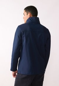 Jachetă bleumarin cu guler înalt, mâneci lungi și un material neted, rezistent la apă. Prezintă o croială lejeră și detalii de design minime.