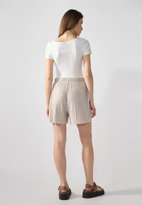 Shorts plissés beiges avec une taille élastique, associés à un t-shirt blanc ajusté et des sandales à plateforme noires, vus de dos.