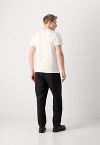 Camiseta corta de manga corta color crema y pantalones negros. La camiseta tiene un escote redondo, y los pantalones son holgados con una textura suave.