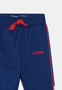 Modré tepláky s červeným šňůrkami a logem Levi's. Po stranách mají kontrastní pruhy v červené a modré barvě. Vyrobeno z měkké bavlny.