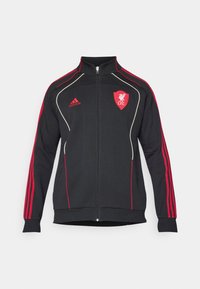 Zwarte zip-up jas met rode strepen en accenten. Bevat een Liverpool FC-logo en Adidas-branding. Zachte textuur met een aansluitend ontwerp.
