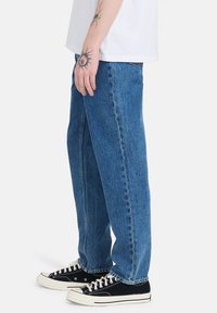 Jeans de mezclilla azul claro con un corte holgado, que presentan un diseño de pierna recta, costuras en contraste y bolsillos. Llevados con zapatillas negras.