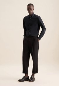 Camicia nera con bottoni e taglio aderente, abbinata a pantaloni neri a vita alta e scarpe di pelle nere. Tessuto liscio con un design su misura.