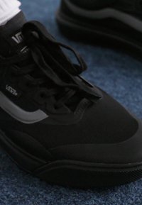 Black athletic shoe with a mesh upper, prominent laces, and a white side logo. The sole features textured rubber for grip.