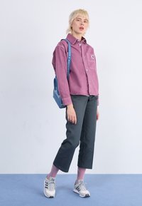 Ljust lila denimskjorta med bröstficka, mörkgrå cropped byxor, rosa randiga strumpor och grå sneakers. Blå väska med textrem.