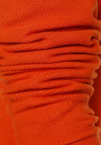 Tissu tricoté orange avec un motif texturé en nid d'abeille, montré en gros plan avec des plis et des rides.