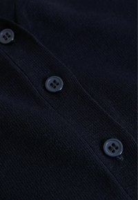 Nærbillede af mørkeblå strikket stof med tre matchende firehuls knapper syet i en lodret række.