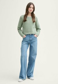 Suéter de canalé verde claro con mangas largas, combinado con pantalones vaqueros de pierna ancha de cintura alta en azul claro y zapatillas blancas.