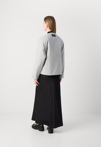 Grå cropped jakke med svart krage, kombinert med et langt svart skjørt. Jakken har en teksturert overflate og en integrert etikett bakerst.