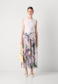 Gonna maxi plissettata con un motivo floreale ad acquerello in colori pastello; abbinata a un top aderente bianco e una borsa gialla.