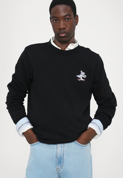 Black crewneck sweatshirt made of cotton, featuring a front embroidered design of a cartoon character on a skateboard. Blue denim jeans.
