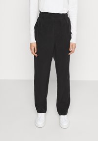 Zwarte wijde broek met een elastische tailleband, gemaakt van een zachte stof. Gecombineerd met witte sneakers voor een contrast in kleur.