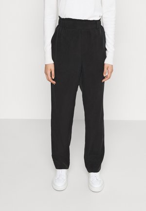 Pantalons larges noirs avec une taille élastique, fabriqués dans un tissu doux. Associés à des baskets blanches pour un contraste de couleur.