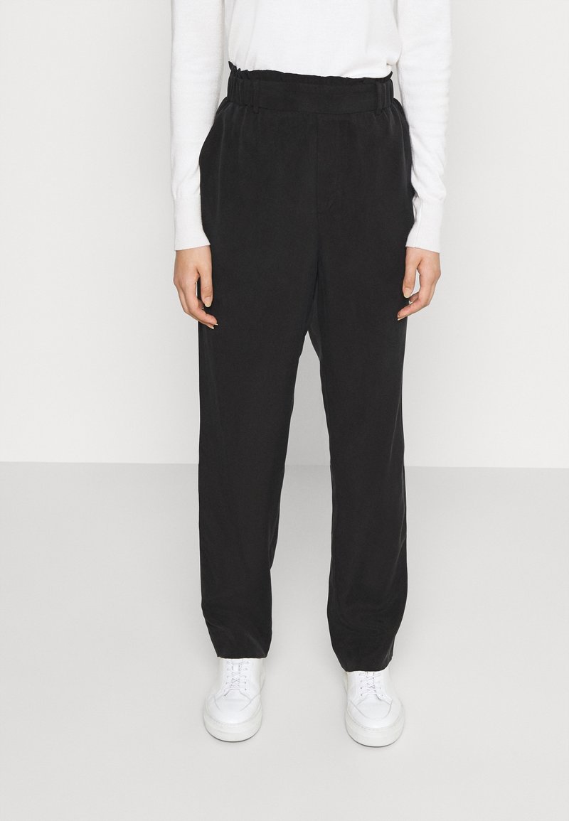 Zwarte wijde broek met een elastische tailleband, gemaakt van een zachte stof. Gecombineerd met witte sneakers voor een contrast in kleur.