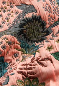 Roze geborduurde stof met ingewikkelde bloem- en vogeldesigns in groene en zwarte draden, met een gestructureerde, zachte afwerking.