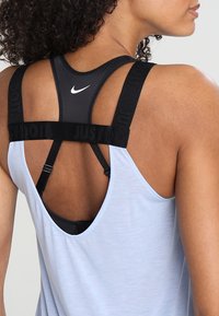 Černé atletické tílko s nápisem "JUST DO IT" na ramínkách, nošené přes světle modré tílko bez rukávů. Má kulatý výstřih a otevřený zadní díl.