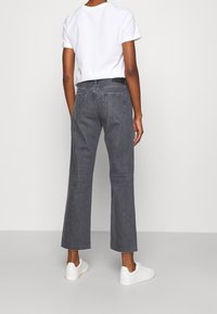 Jeans wide-leg in denim grigio con orlo sfrangiato, dotati di due tasche posteriori. Abbinati a una T-shirt bianca semplice e scarpe da ginnastica bianche.