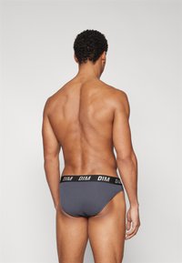 Graue Baumwollunterwäsche mit einem schwarzen Bund, der das Branding "DIM" trägt, enganliegendes Design und minimale Abdeckung, von hinten gezeigt.