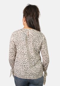 Blusa ligera de manga larga con un patrón de leopardo en beige y gris, con cierre en la espalda tipo ojal y puños atados. Textura suave y lisa.