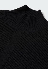 Pull-over à col roulé en maille côtelée noire, présentant un col plié et des lignes verticales texturées en vue rapprochée.