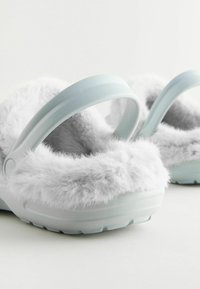 Weiche, hellblaue Holzschuhe mit einem flauschigen grauen Futter und einer geformten Gummisohle. Verfügt über einen gebogenen Riemen für einen sicheren Sitz.