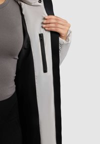 Padded jacket featuring a black and light gray color scheme, with a zip pocket and a smooth, lightweight fabric.