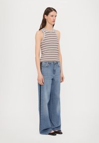 Stripet uttenert topp i brunt og krem paired med vide blå jeans. Antrekket har en avslappet passform og minimalistisk design.