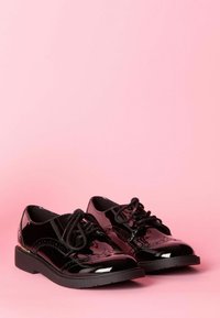 Scarpe in pelle verniciata nera con lacci e dettagli brogue, punta tondeggiante e suole in gomma nera, su uno sfondo rosa.