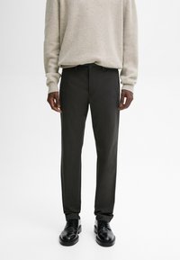 Pantalons gris foncé à coupe droite, avec une texture lisse, passants pour ceinture et poches avant, assortis à un pull clair et des chaussures noires.