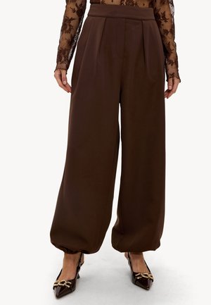 Pantalon marron taille haute à jambes larges avec ourlets froncés, porté avec un haut à manches longues en dentelle florale transparente et des escarpins à bout pointu avec un détail chaîne en or.