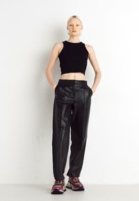 Fekete rövidített tank top, amelyet magas derekú fekete bőr nadrággal párosítottak. A lábbeli tömör kialakítással rendelkezik, rózsaszín és szürke részletekkel.