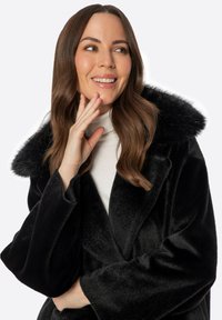 Abrigo de piel sintética negro con un cuello ancho, textura suave y corte holgado. Presenta un diseño de solapa y una silueta limpia y elegante.