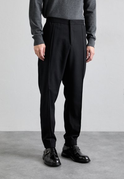 Pantalons noirs ajustés avec une coupe fuselée, en tissu lisse. Comprend une taille élastique et des ourlets à revers, associés à des chaussures noires.