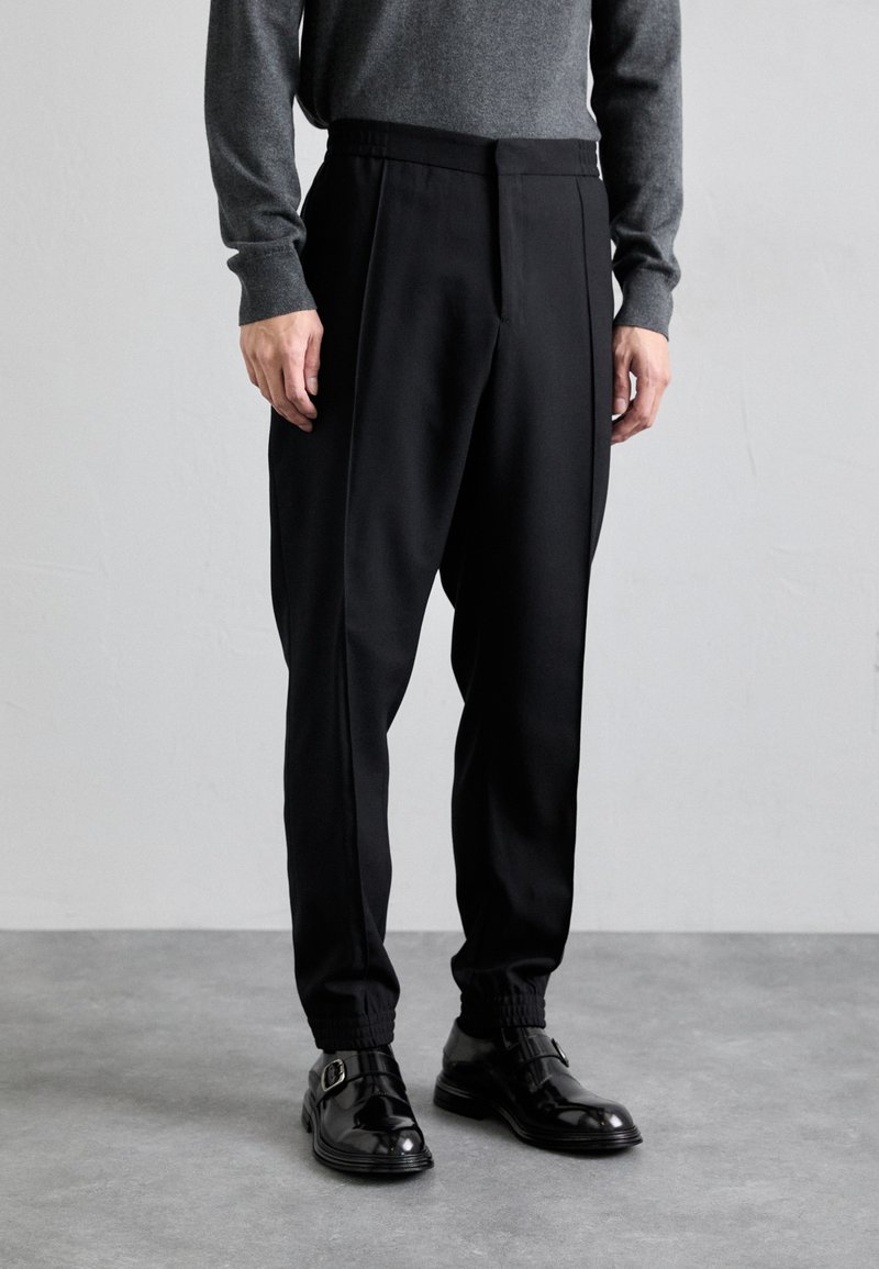 Pantalones negros ajustados con un corte entallado, hechos de una tela suave. Cuentan con una cinturilla elástica y dobladillos acampanados, combinados con zapatos negros.