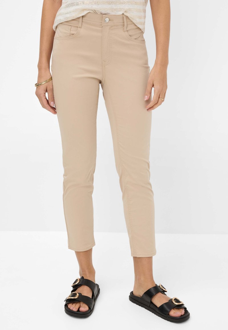 Beige, slim fit broek van een zachte stof met een rits- en knoopsluiting, met voorzakken en een rechte pijpdesign. Zwarte sandalen met gouden accenten.