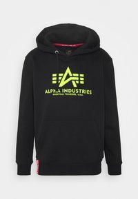 Sudadera negra con capucha de la marca Alpha Industries, logo y texto en amarillo neón que dice "Knoxville, Tennessee, U.S.A." Con bolsillo tipo canguro en la parte delantera y cordón para la capucha.
