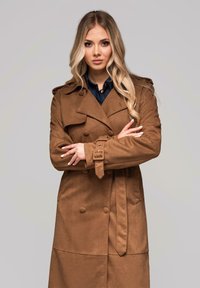 Gabardina marrón de tejido suave, con botones de doble fila, cinturón en la cintura y charreteras en los hombros. Textura lisa, diseño hasta la rodilla.