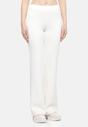 Pantaloni bianchi a gamba larga realizzati in tessuto liscio, con vita alta. Abbinati a sneaker di colore chiaro.