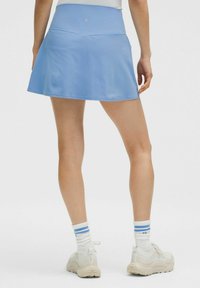 Svijetloplava atletska suknja s pripijenim strukom i lepršavim dizajnom, izrađena od glatkog, rastezljivog materijala, s minimalnim šavnim detaljima.