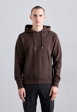 Brun hætte sweatshirt med en frontlomme, snoretræk og ribbede manchetter; båret med sorte bukser mod en ensfarvet baggrund.