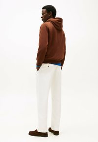 Felpa marrone con cappuccio, pantaloni bianchi, mocassini texture. Outfit casual con una vestibilità rilassata e materiali a contrasto. Vista posteriore mostrata.